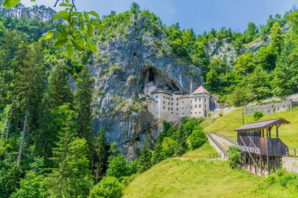 Blick auf die Landschaft und die in die Felswand gebaute mittelalterliche Burg in Predjama, Slowenien, im Sommer